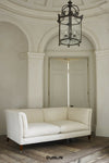 An off-white leather loveseat sofa with dark wooden legs, positioned in a classic European-style room with a domed ceiling, arched doorway, and a hanging black metal chandelier. The brand name 'DUNLIN' is printed in black text at the bottom center.