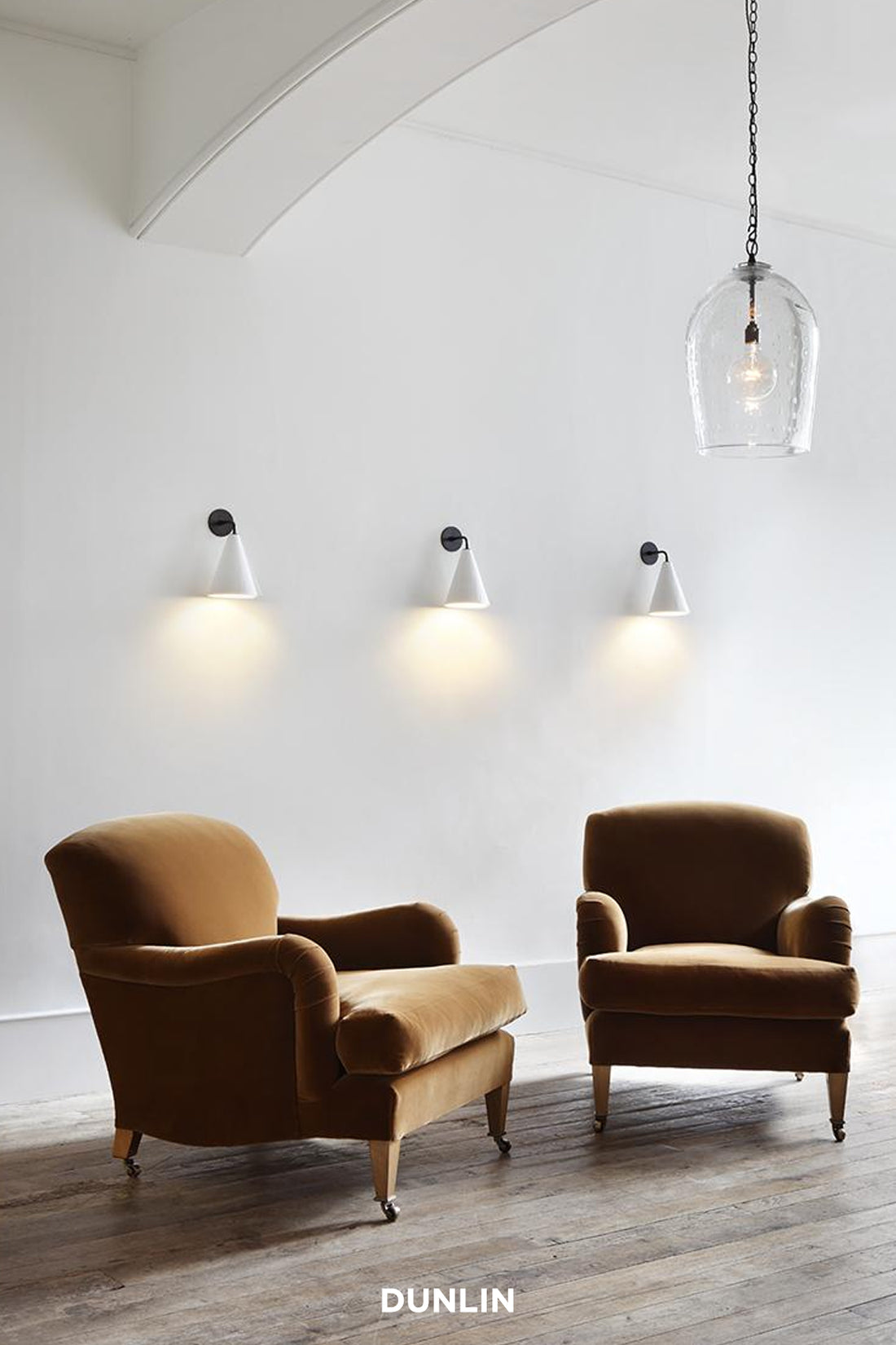 Gingerbread velevt - small Chairs Two brown armchairs in a room with pendant lights and 'Dunlin' branding.