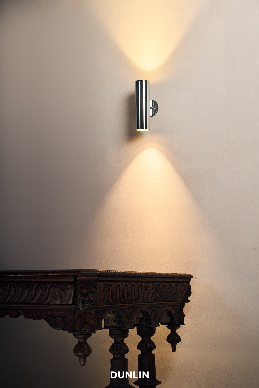 A nickel-plated brass up-down light fixture mounted on a wall, with illumination visible in the vertical and horizontal directions.
