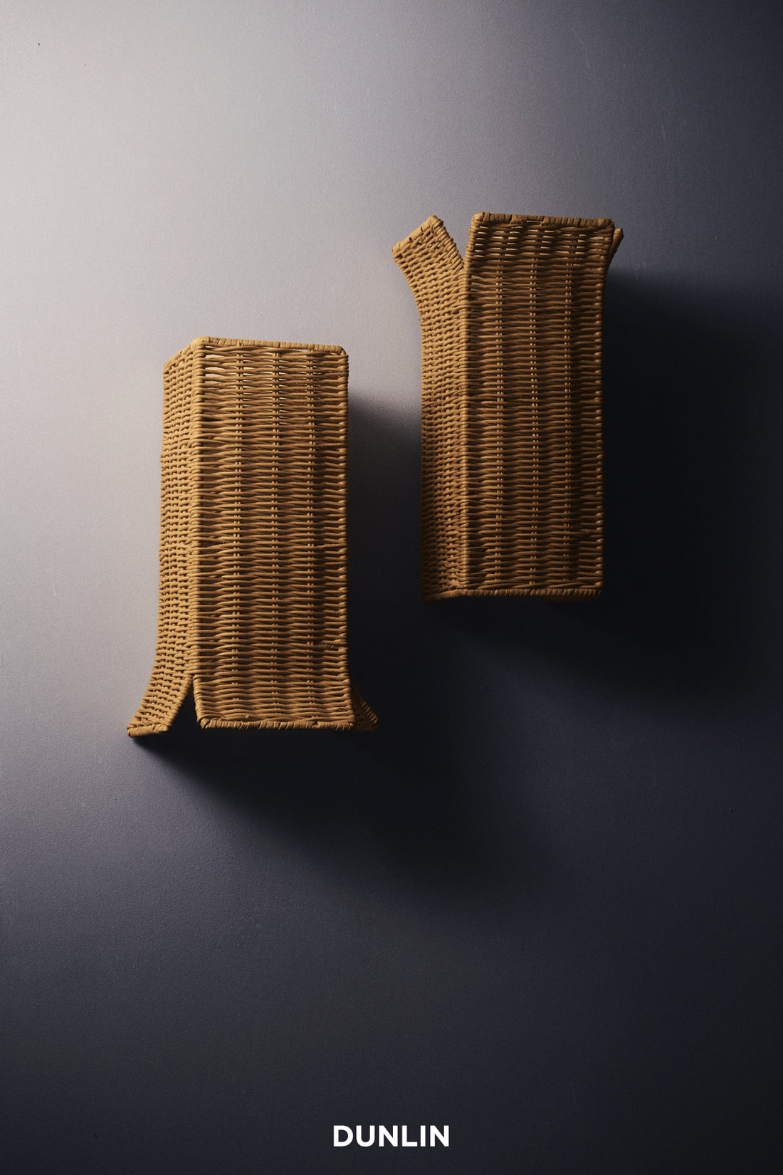 Two Dunlin Filippo rattan wall sconces mounted on a dark wall, with a visible Dunlin logo at the bottom. DUNLIN Rattan UP down lights 