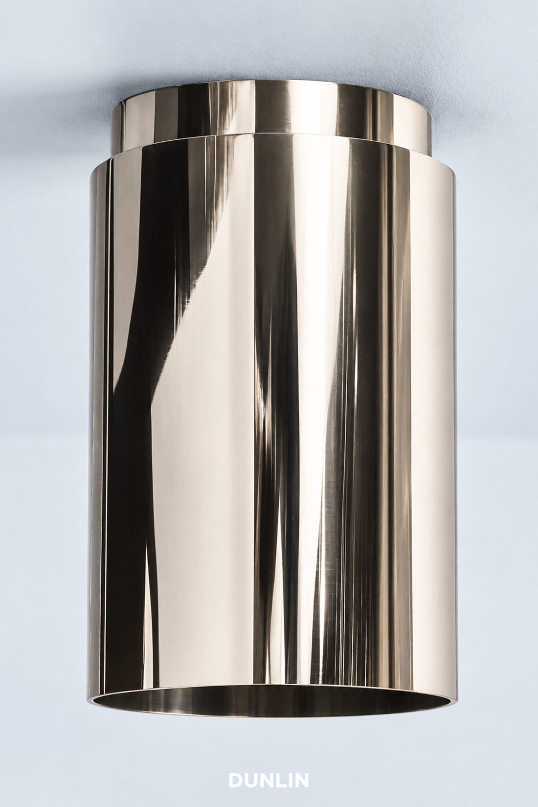 A modern cylindrical wall-mounted light fixture with a highly polished, reflective metallic finish, shown against a light blue background with the brand name 'DUNLIN' at the bottom.