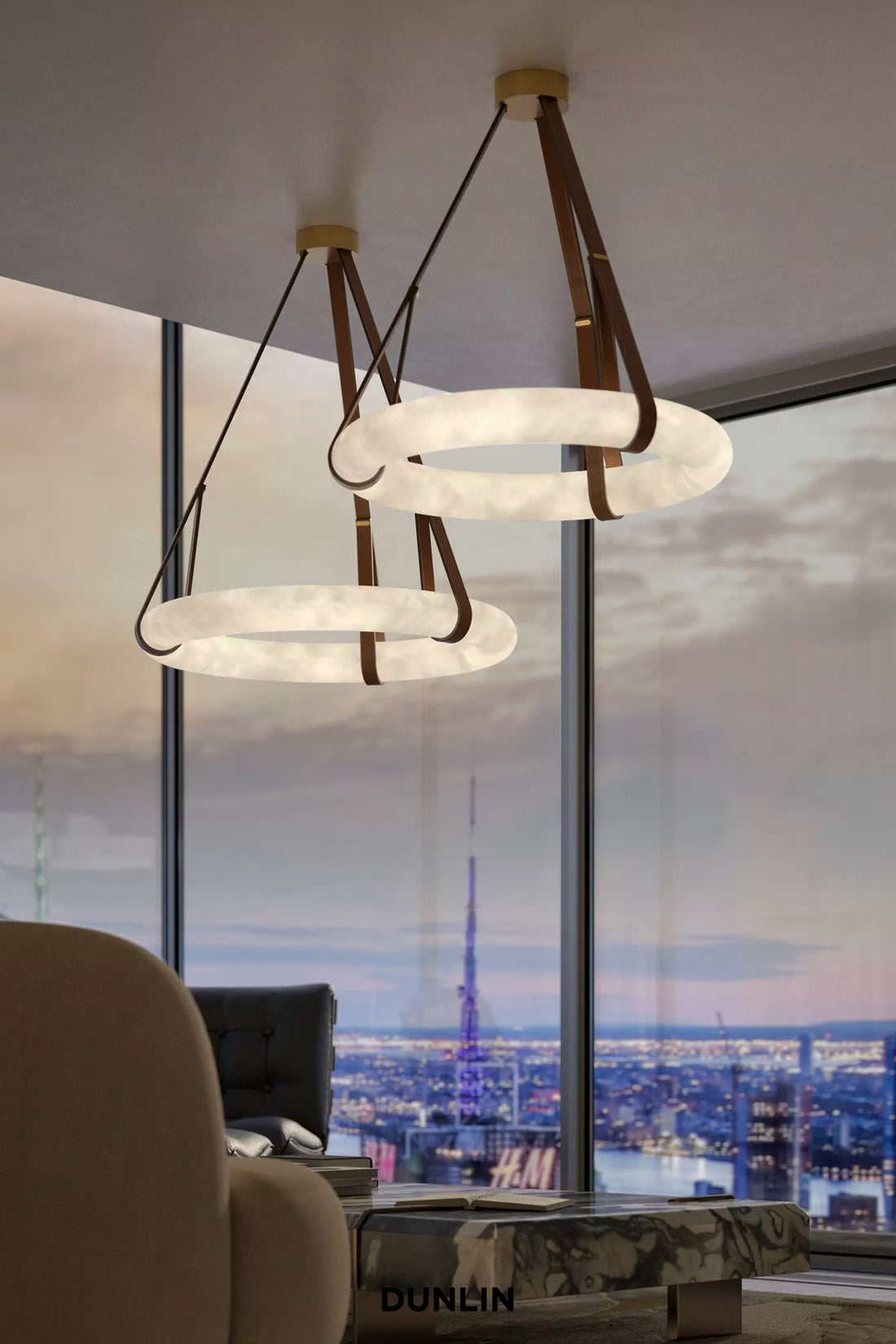 Two modern DUNLIN pendant chandeliers with white textured circular rings and brown leather straps hanging in a high-rise office lobby with a city skyline view.