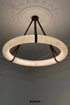 A modern circular pendant light with a glowing warm white textured glass ring and dark metal suspension straps, shown hanging from a decorative ceiling medallion in an interior room. The brand name DUNLIN is printed at the bottom.