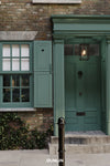 A classic green front door with a black metal lantern light, set in a brick building with matching green shutters and a stone sidewalk. The brand name 'DUNLIN' is printed at the bottom.