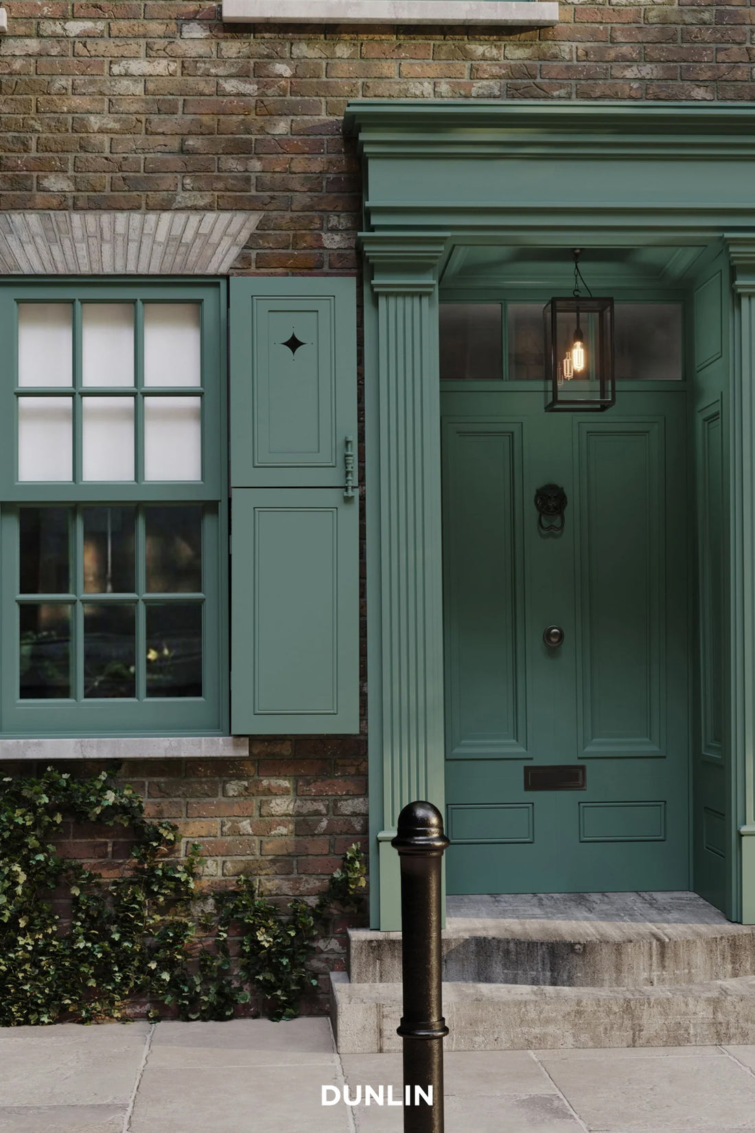 A classic green front door with a black metal lantern light, set in a brick building with matching green shutters and a stone sidewalk. The brand name 'DUNLIN' is printed at the bottom.