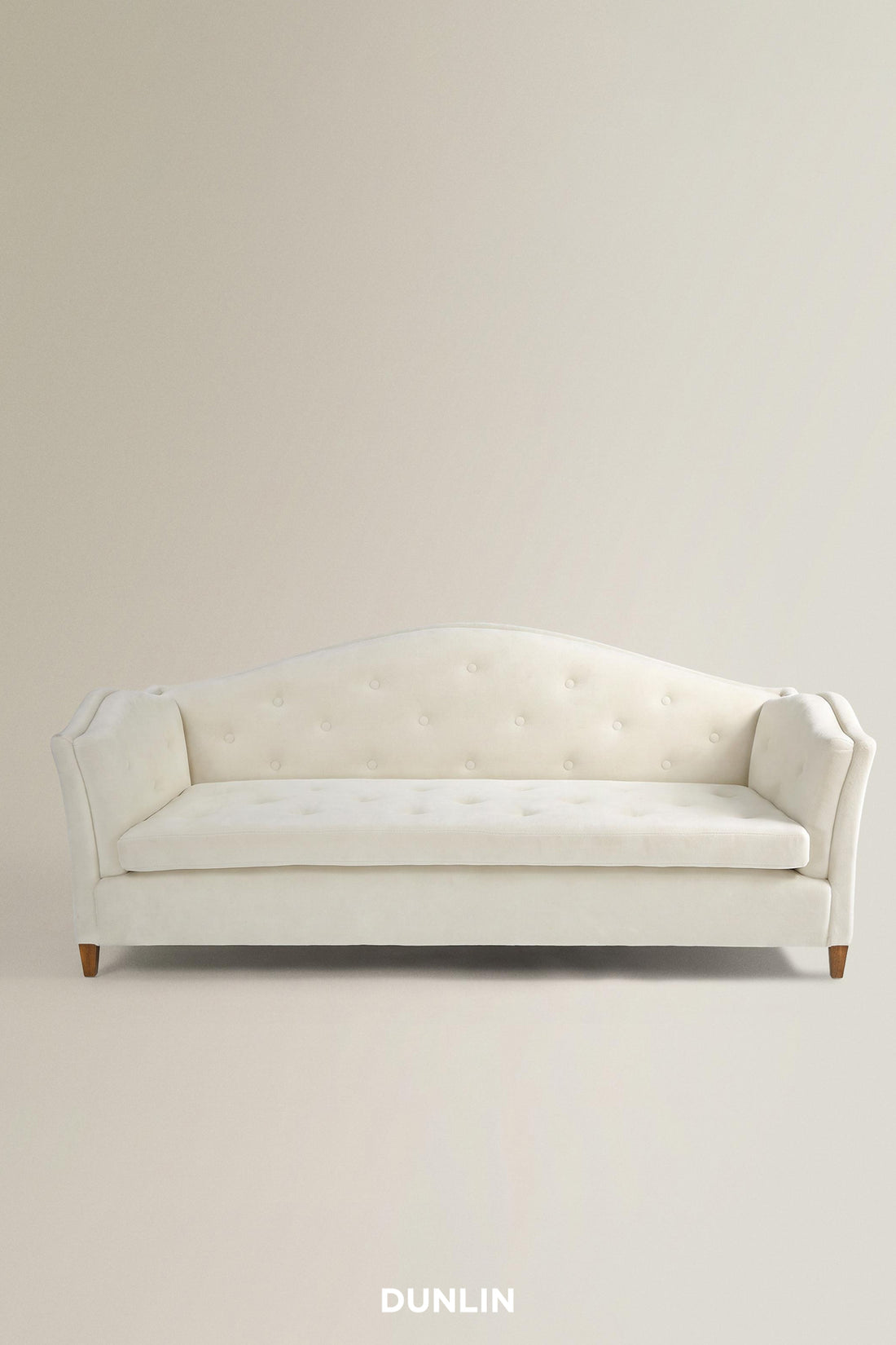 An off-white tufted loveseat sofa with a curved backrest and small wooden legs, shown against a plain beige studio background with the brand name DUNLIN at the bottom.