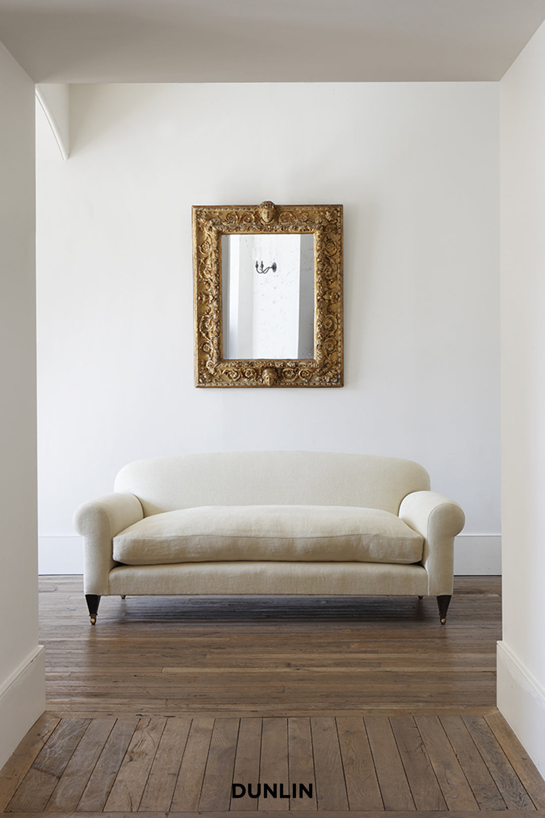 Beige sofa in a room with a decorative mirror on the wall, featuring the brand 'Dunlin'.