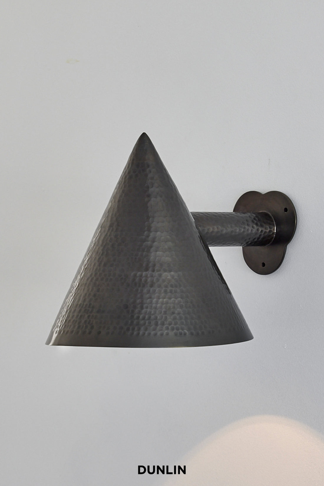 A weathered brass wall light with a conical shape and a petal wall plate, branded by Dunlin.