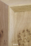Close-up of a light natural wood cabinet corner showing grain and a burl pattern, with the word DUNLIN at the bottom.