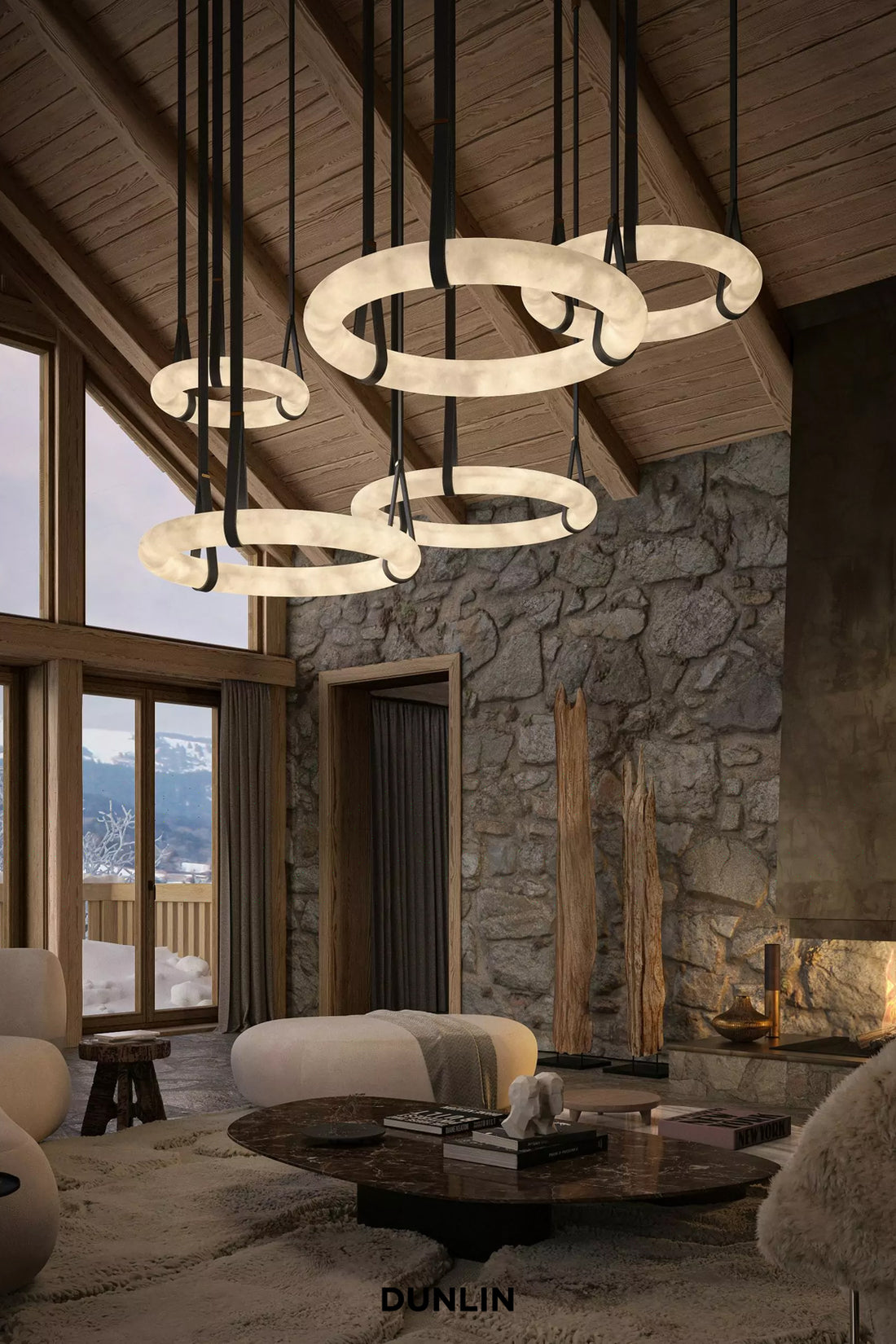 A luxury modern chandelier with multiple interlocking circular ring lights in a rustic mountain chalet living room. The brand name 'DUNLIN' is visible at the bottom.